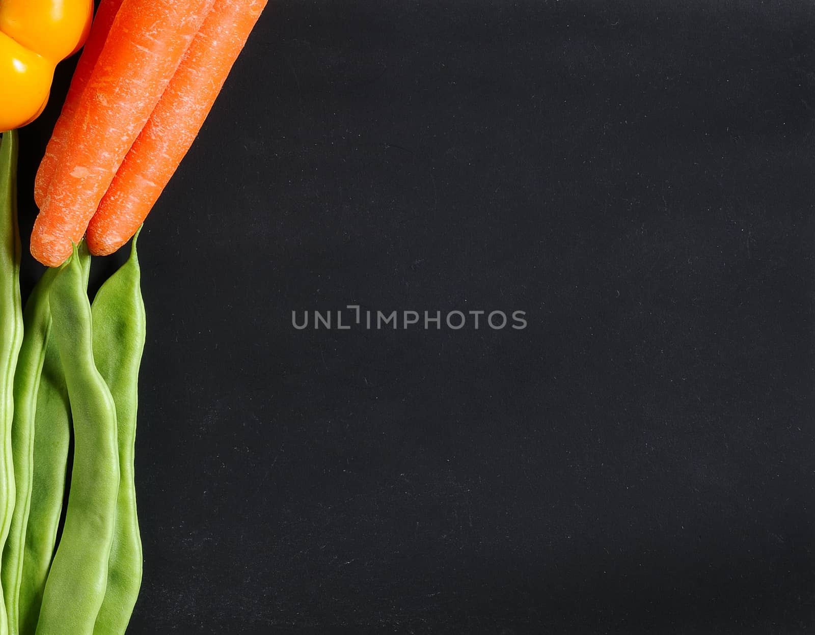 Fresh vegetables as carrots, beans and peppers on a blackboard.