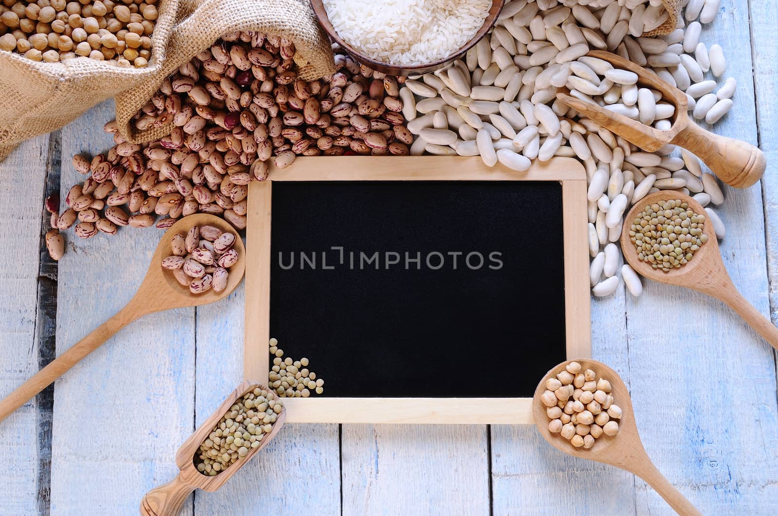 Different types of beans around black framed square on blue wooden table. From above.