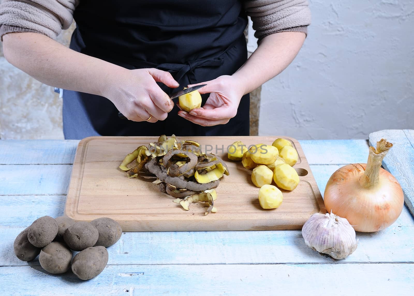 Peeling potatoes on wooden table in the kitchen.