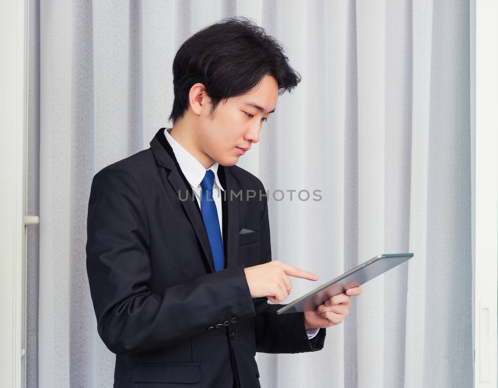 Work from home, Asian young businessman wear suit video conference call or facetime he smiling using smart digital tablet computer and point finger on the screen at home office, looking to tablet