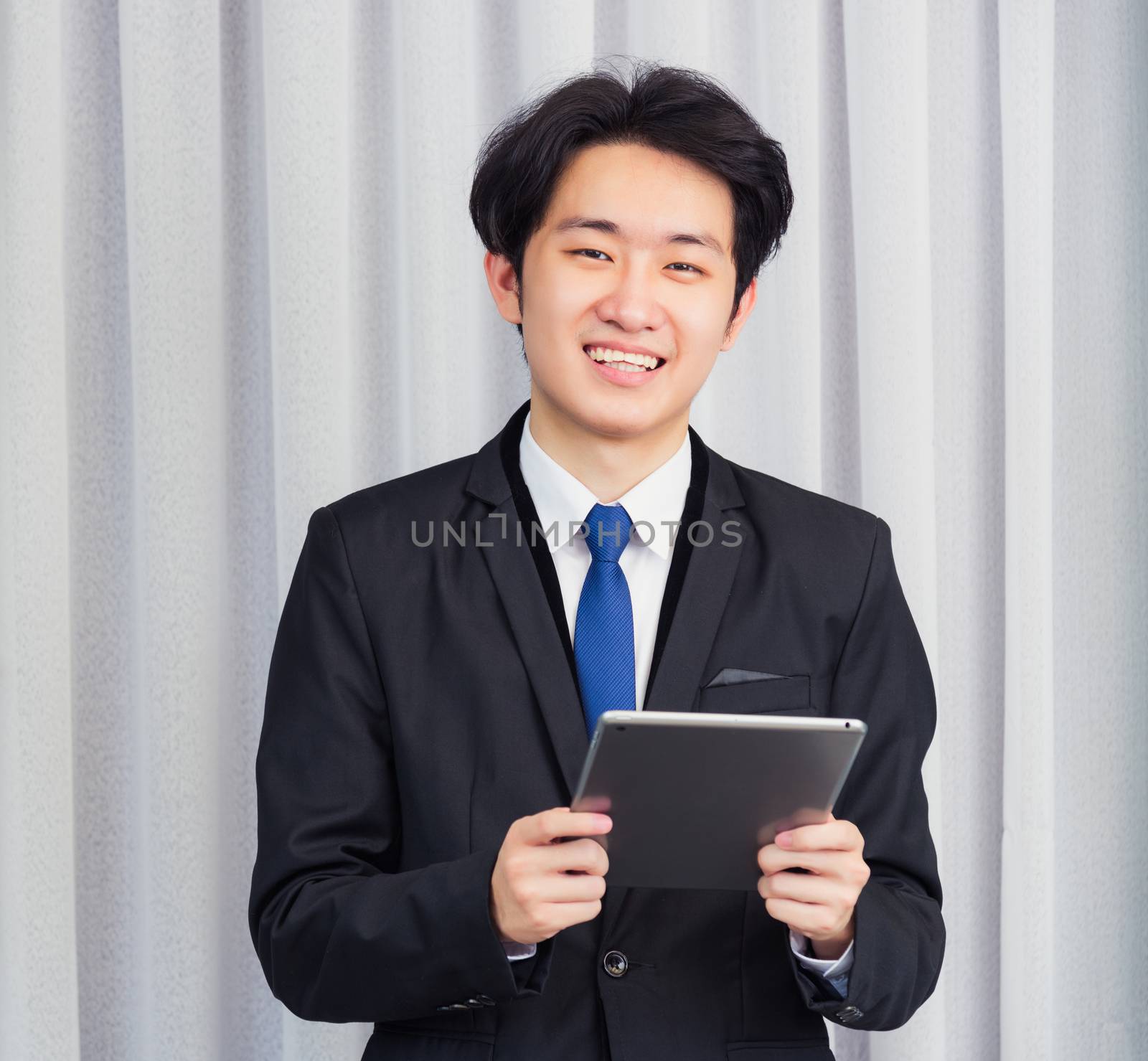 Work from home, Asian young businessman wear suit video conference call or facetime he smiling using smart digital tablet computer touching on screen at home office, looking to camera