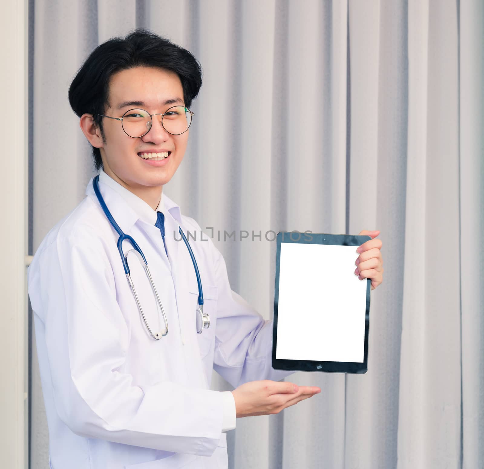 Portrait closeup of Happy Asian young doctor handsome man smiling in uniform and stethoscope neck strap showing front blank screen smart digital tablet on hand, Healthcare medicine concept