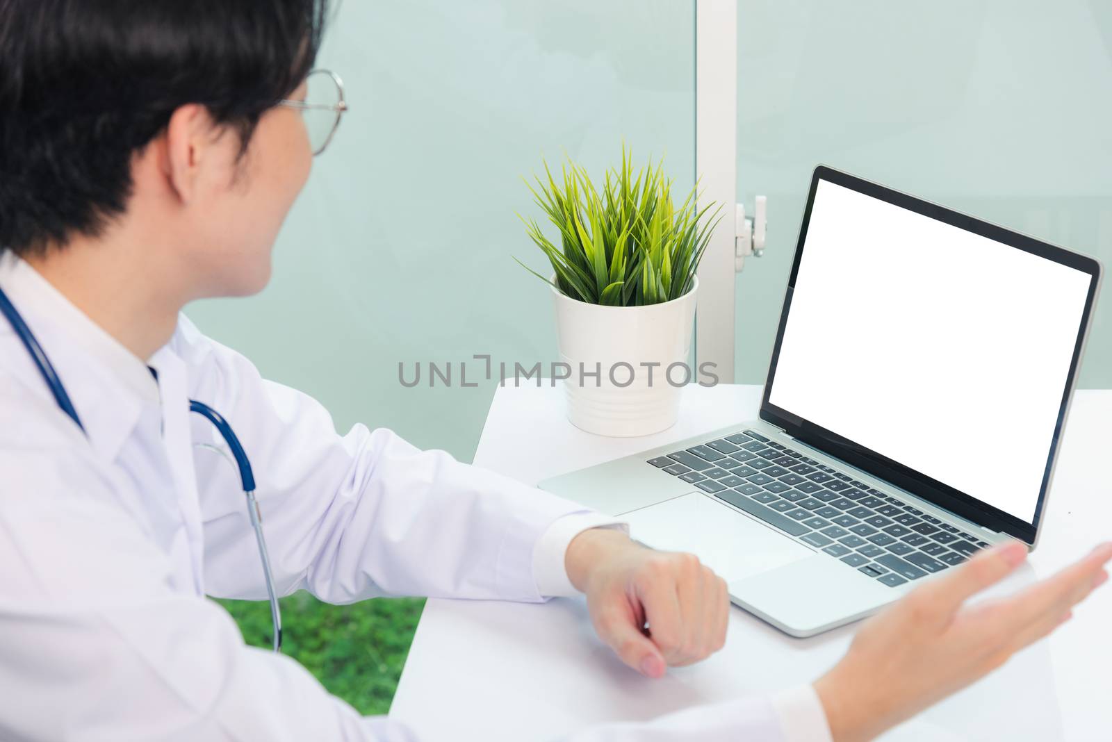 Asian young handsome doctor man wearing a doctor's dress and stethoscope video conference call or facetime raise hand to explain the symptoms he smiling at hospital office, Health medical care concept