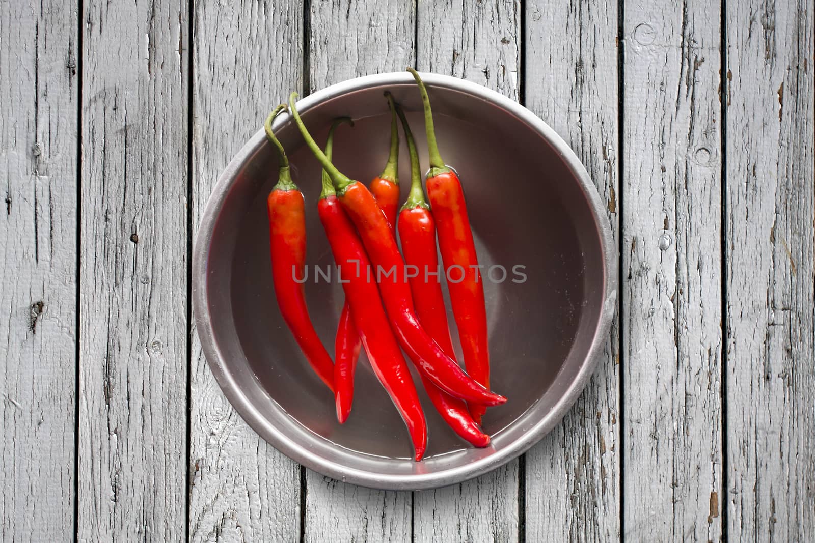 Fresh red chilli pepper in water on bowl of steel on grey wooden background,copy space, Overhead view of chili pepper on wood background