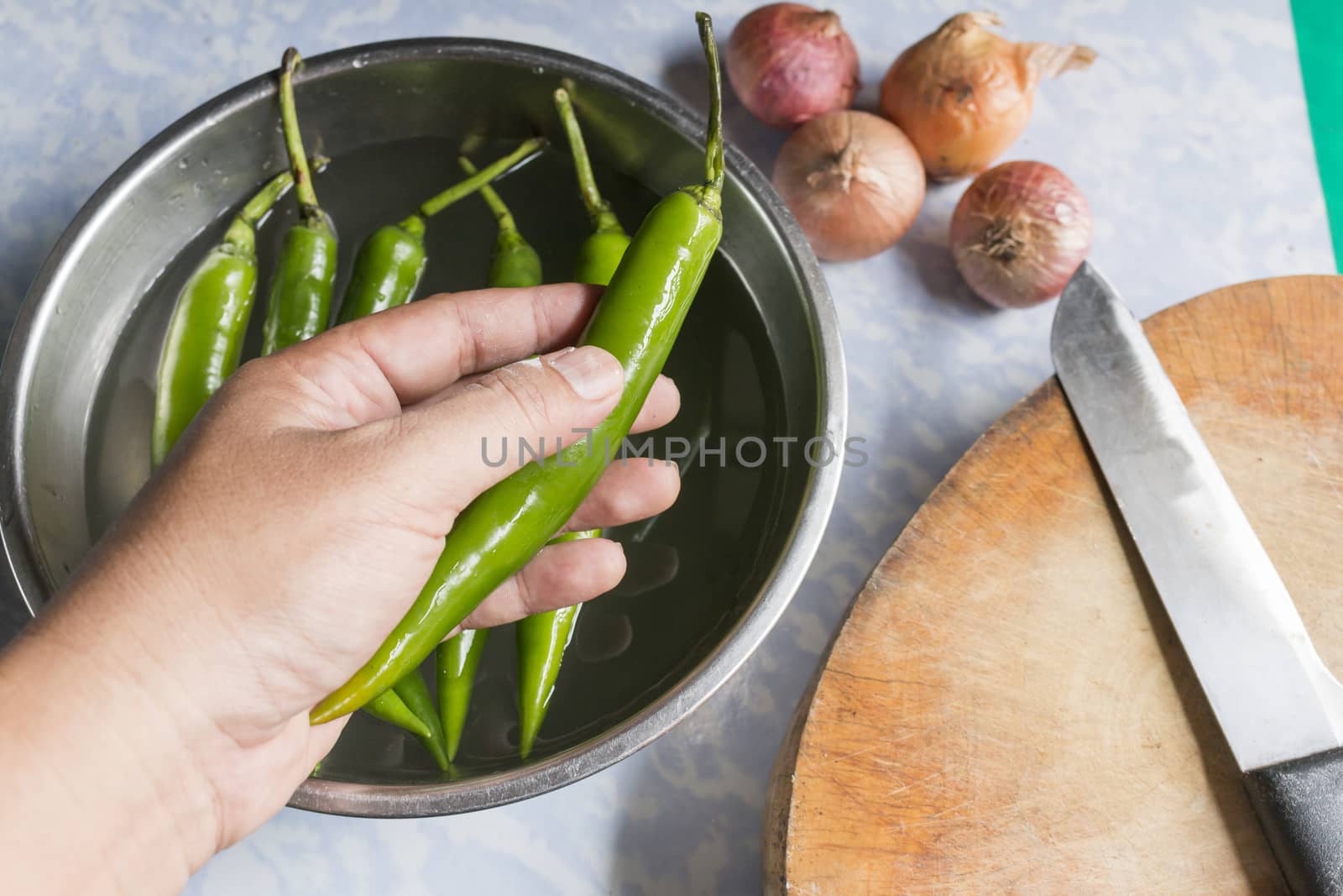 Chef hand holding green chilli pepper for cutting in kitchen,food concept