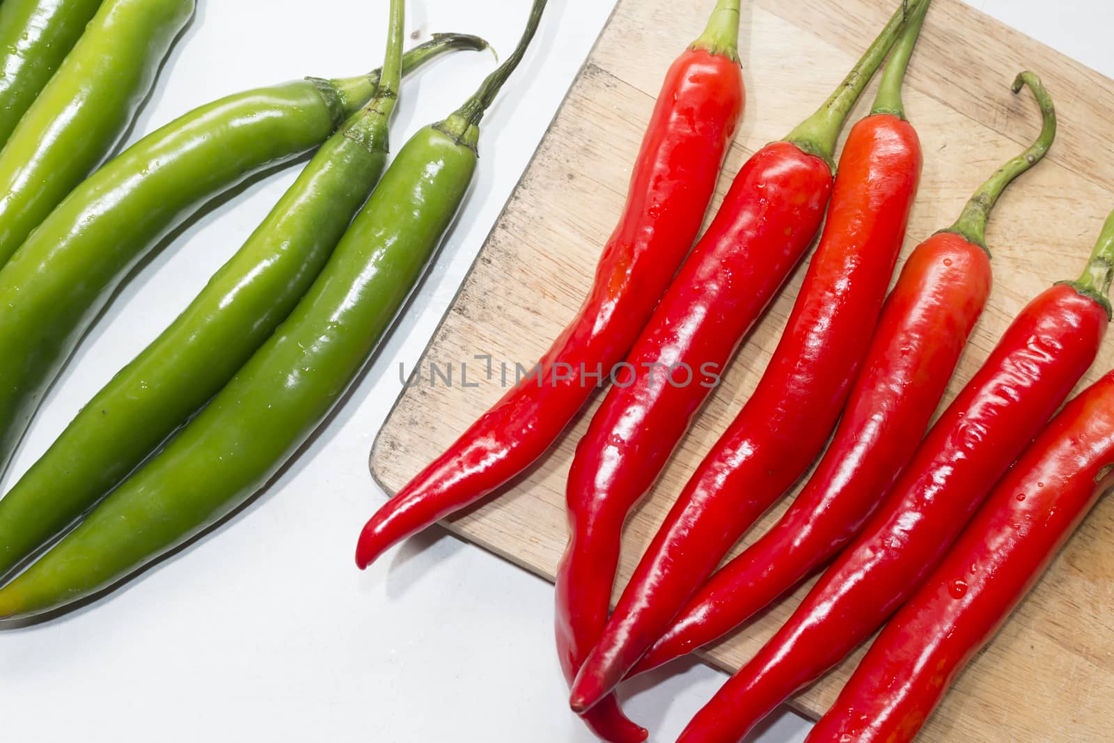 red chilli on cutting board with green chilli on white table,top view