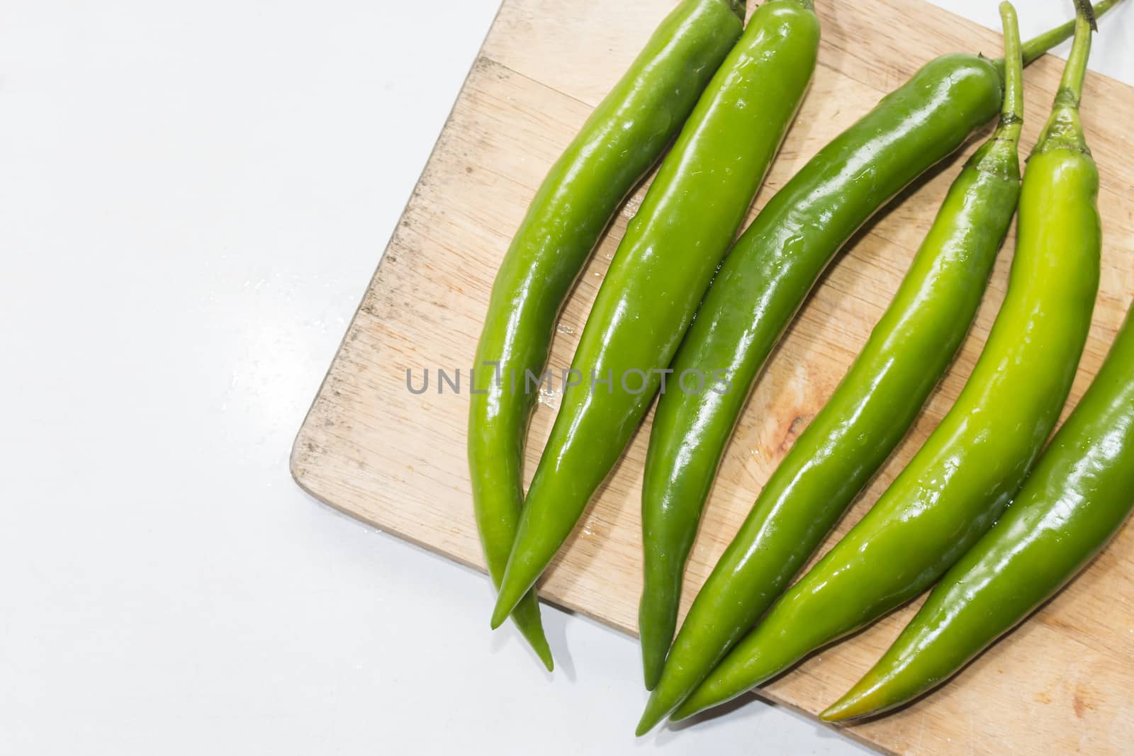  green chilies on a wooden cutting board.