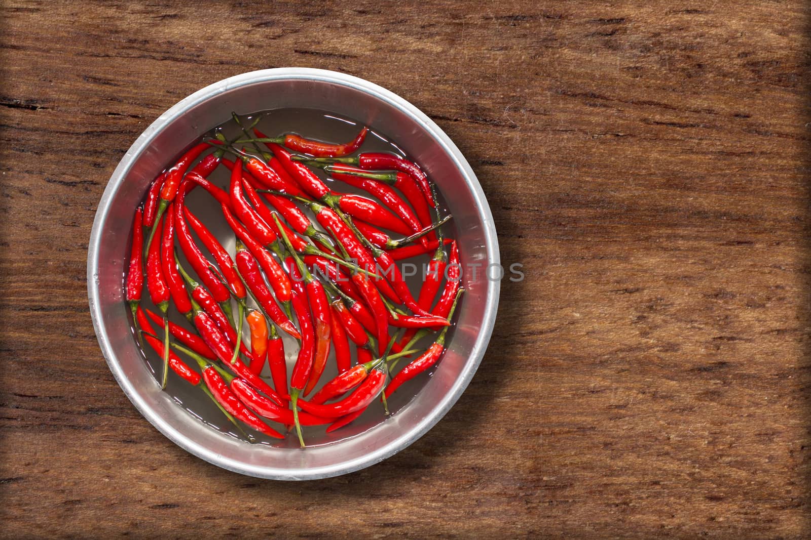 Top view of red chilli pepper in water on bowl of steel on wooden background,copy space