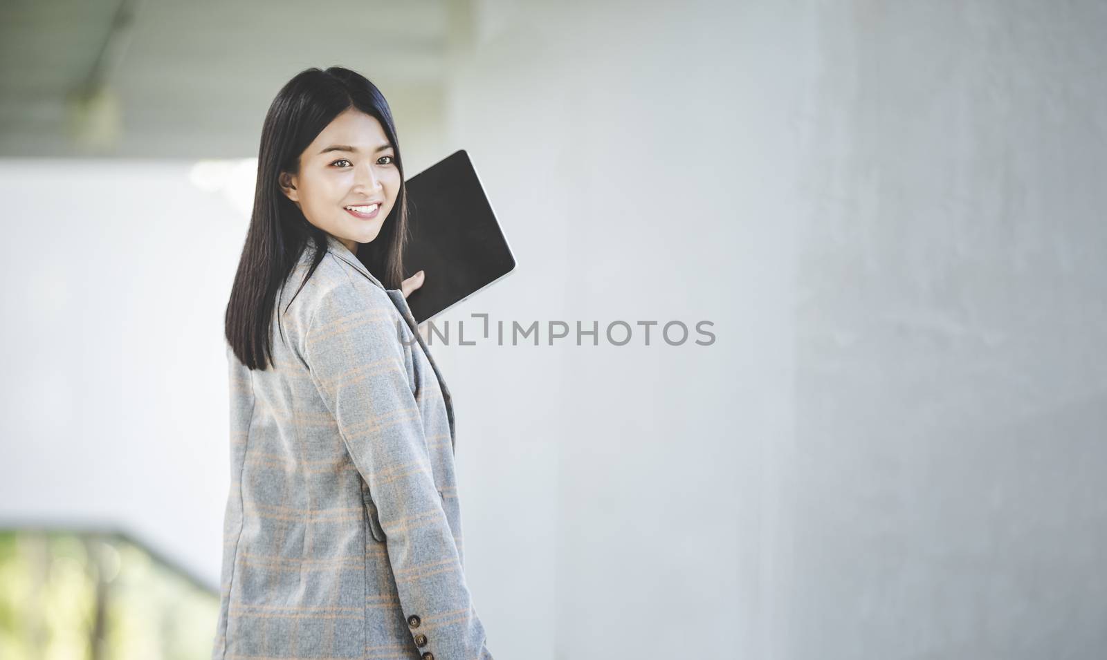 Portrait of business woman looking digital tablet with white travel bag on walkway while waiting to travel to the destination 