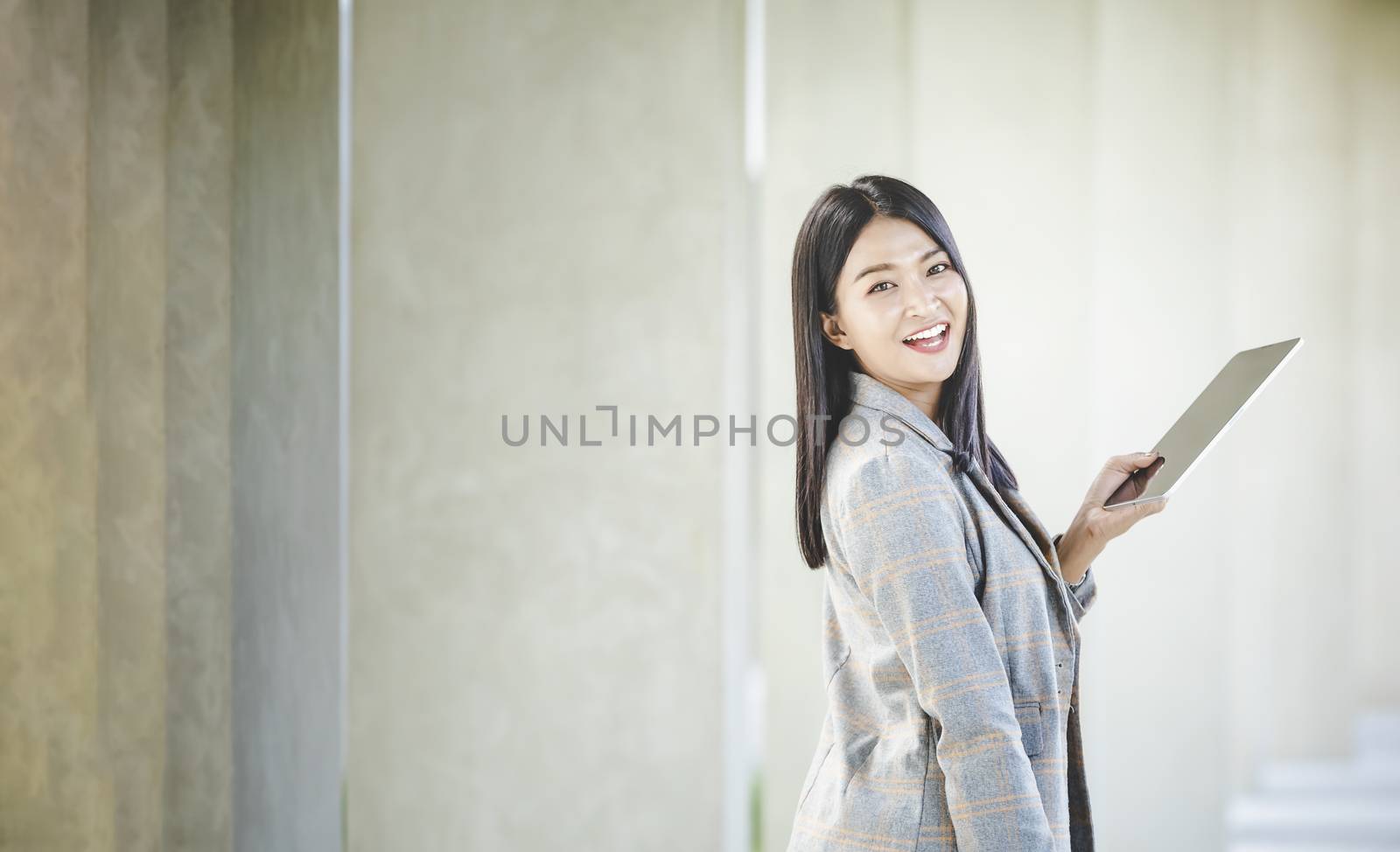 Portrait of business woman looking digital tablet with white travel bag on walkway while waiting to travel to the destination 