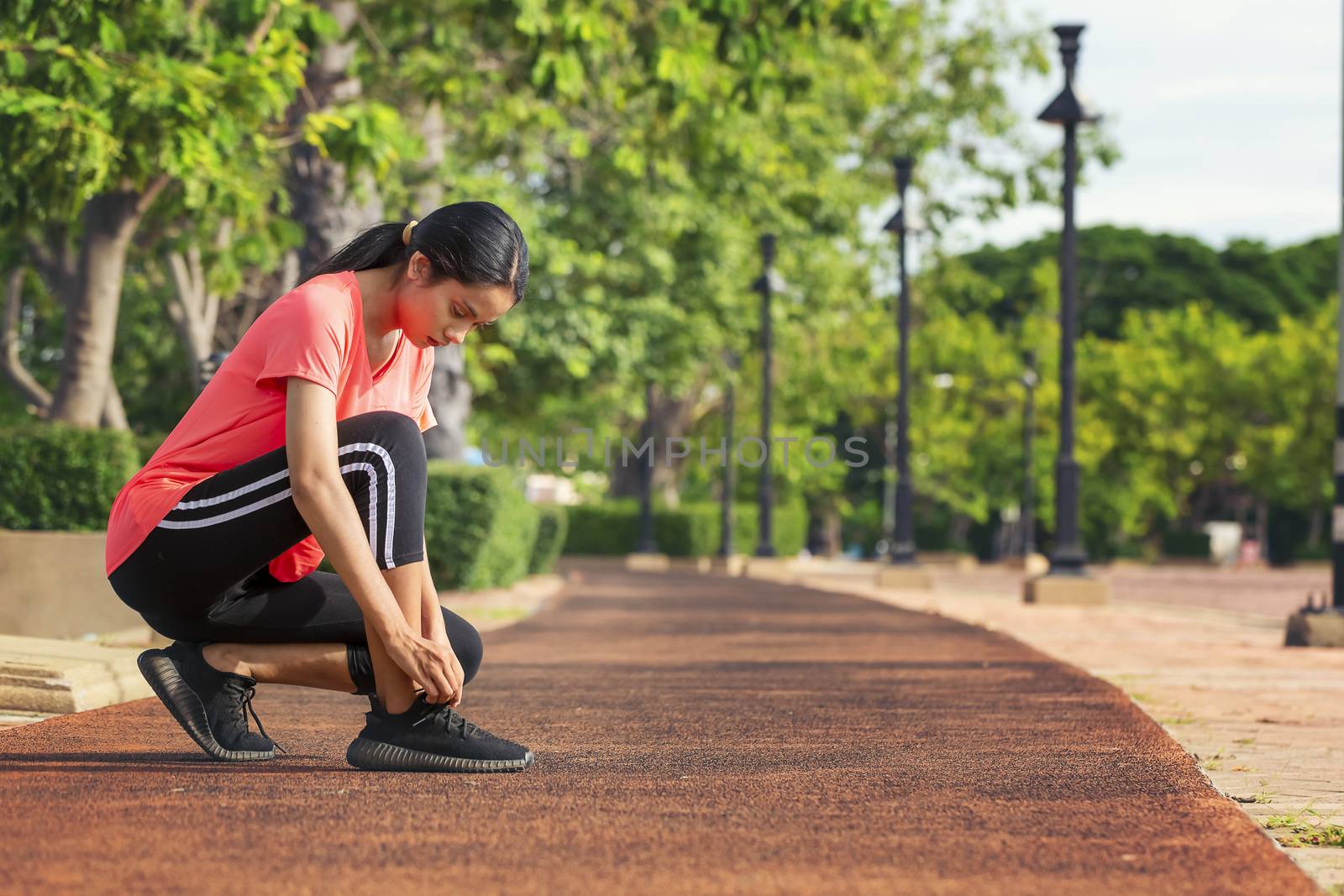 Beautiful woman is lacing a running shoe on the runway in the park before exercising for health care. Healthy concept