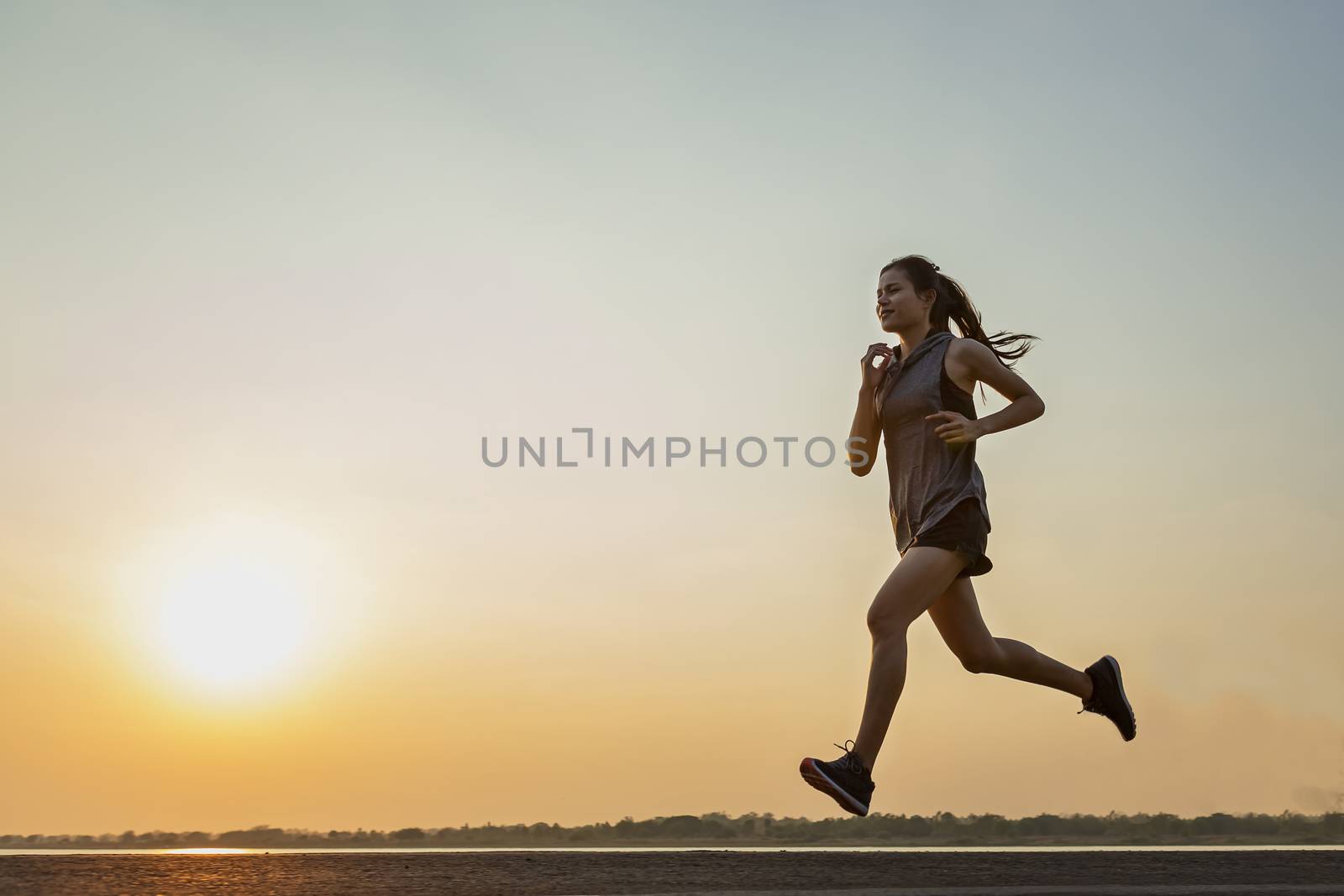 The silhouette of young women running and exercising at sunset with the sun in the background, colorful sunset sky
