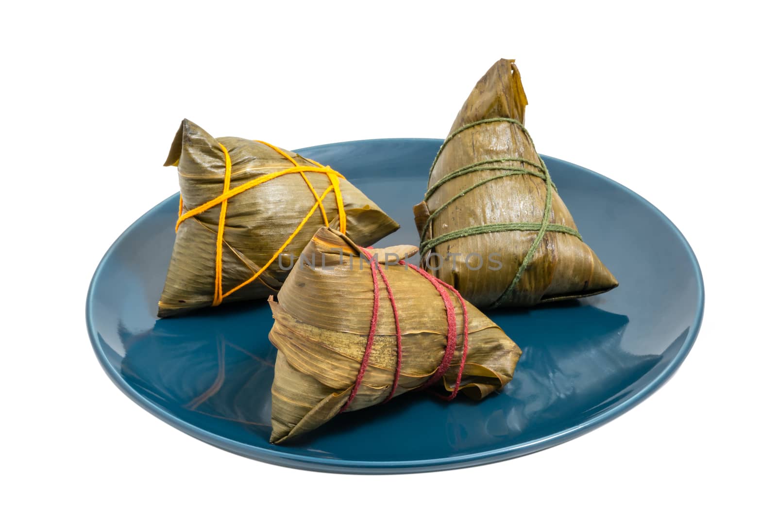 Three ZhongZi - traditional Chinese rice dish in bamboo leaves on a blue plate isolated on white