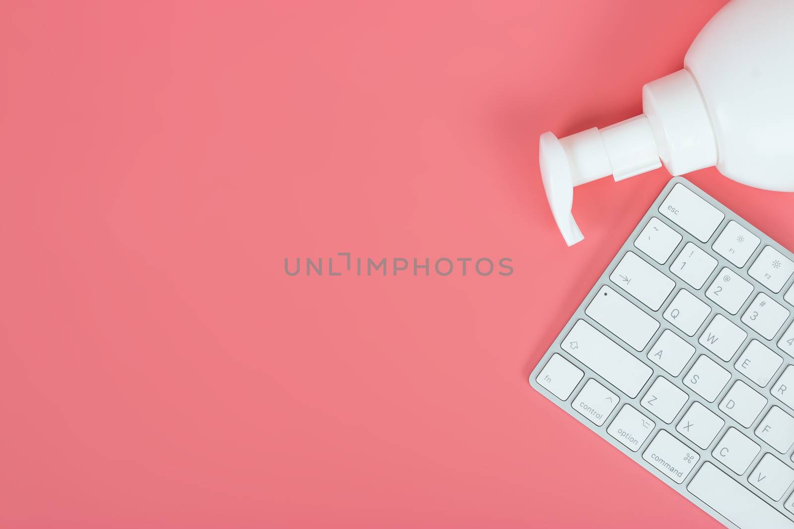 Flat lay, top view office table desk. Workspace with keyboard and hand Sanitizer on pink background.