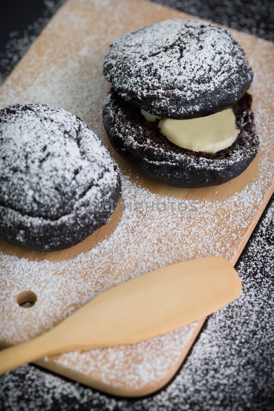 Donut with icing sugar topping on wooden plate.