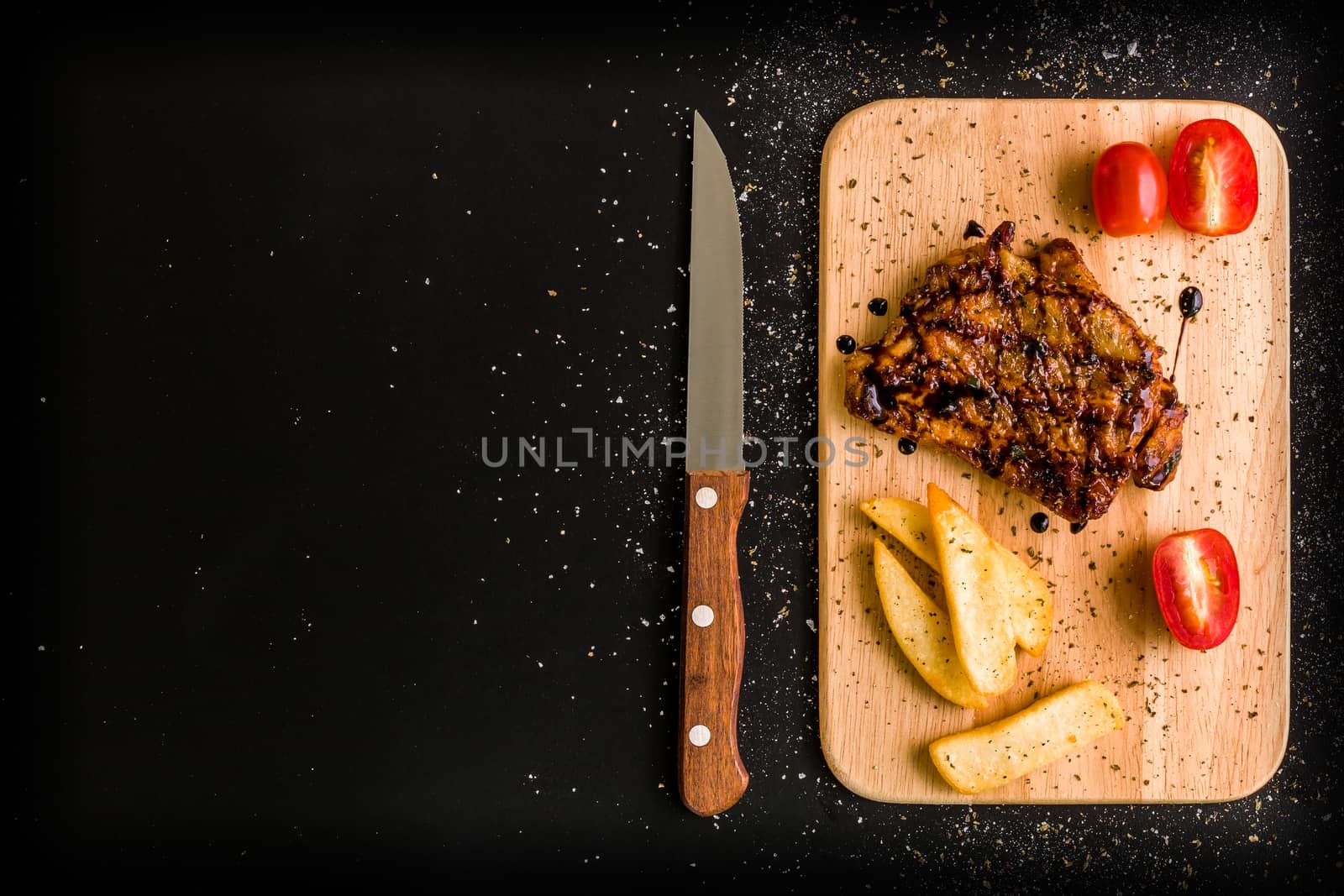 Grilled chicken steak on wooden cutting plate on black background.