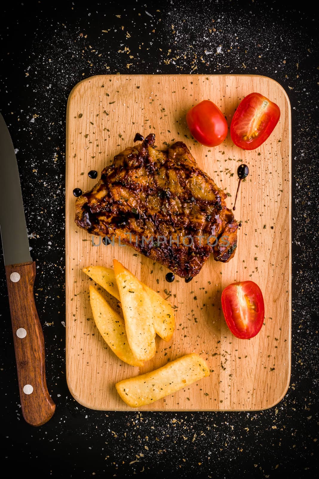 Grilled chicken steak on wooden cutting plate on black background.