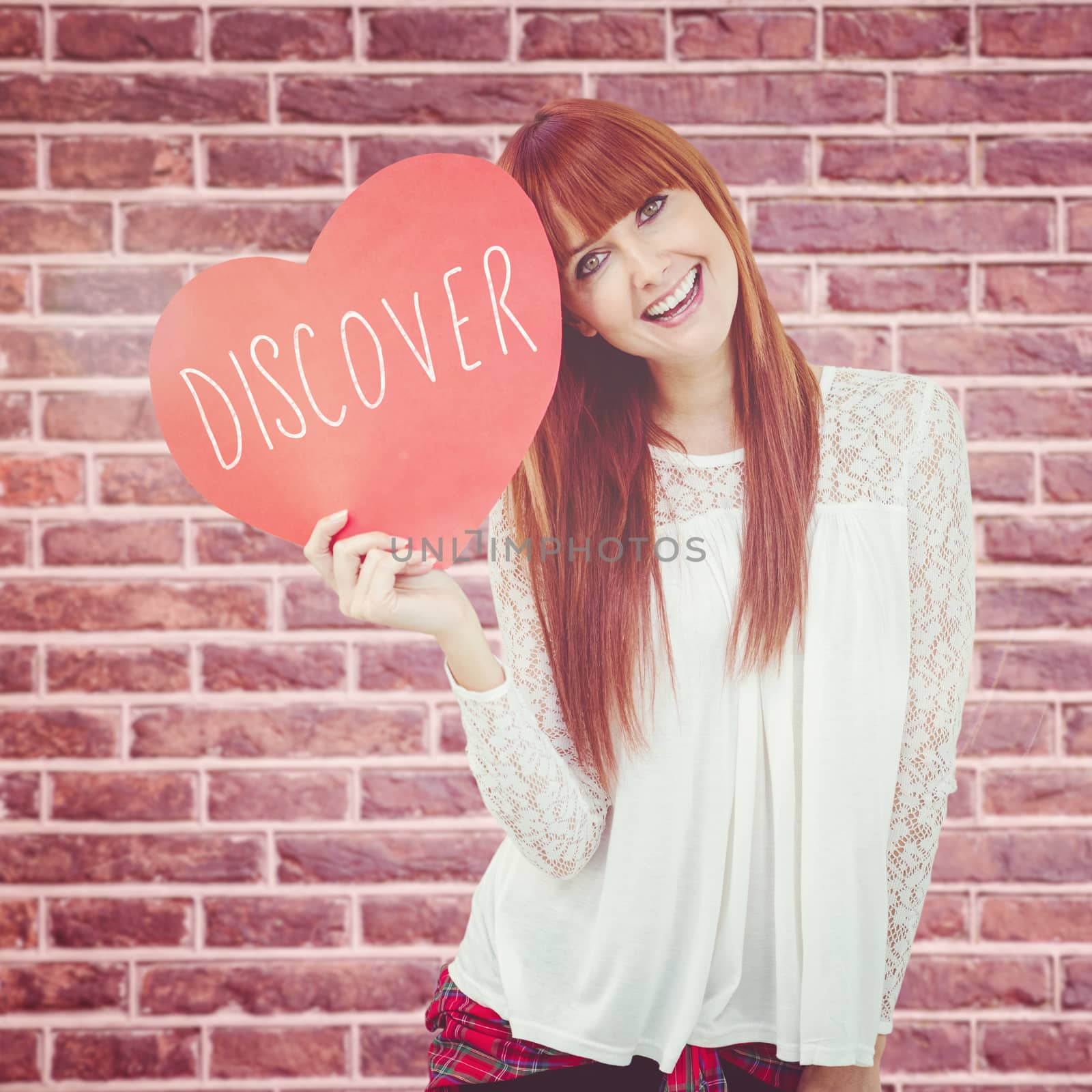 Smiling hipster woman with a big red heart against red brick wall