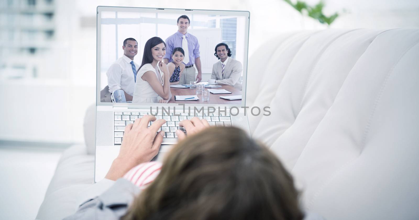 Woman using laptop while lying on sofa against international business associates in a meeting