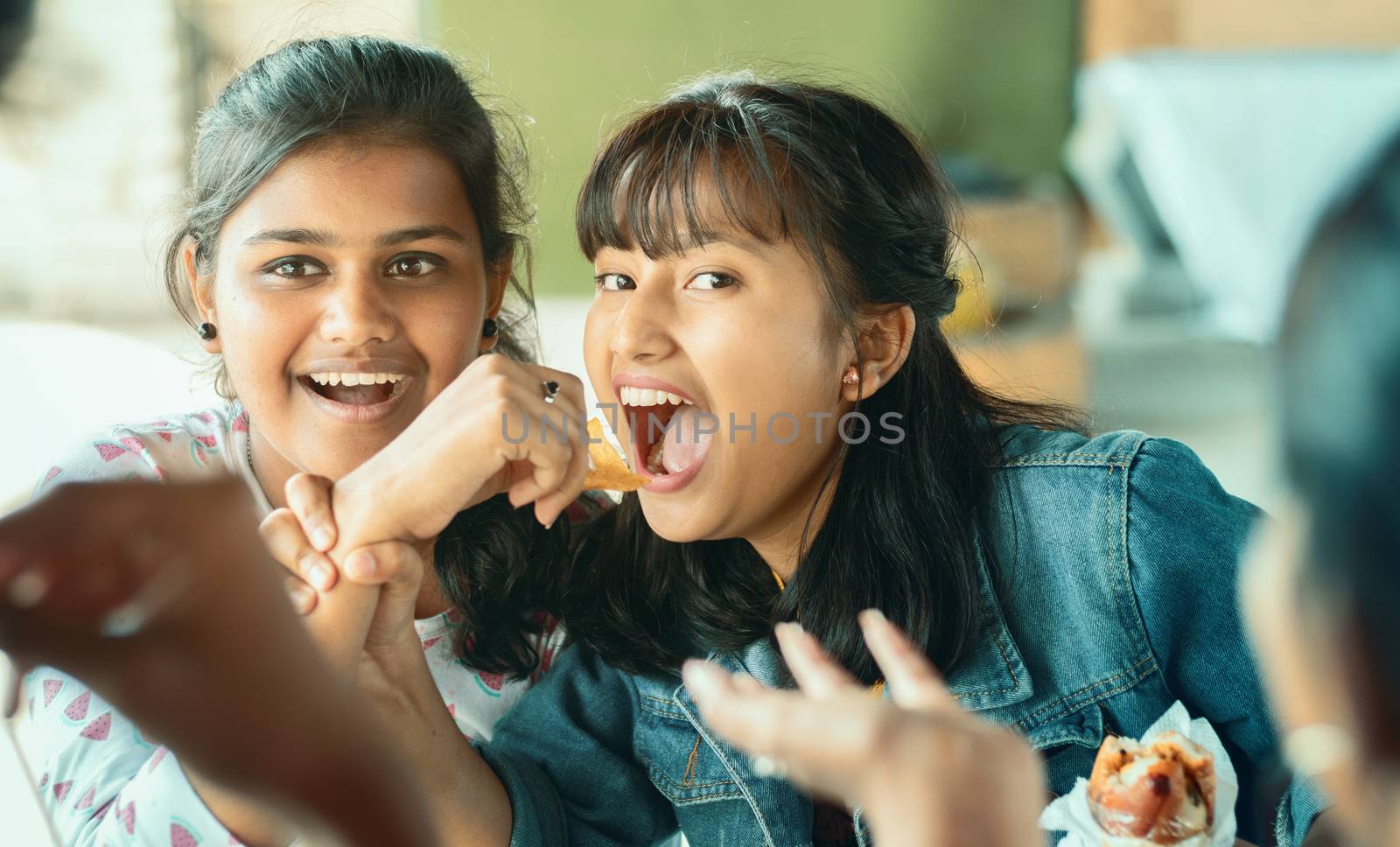 Teenager trying to take or grab food from friend - young girl playfully fighting for snacks with her friend - concept of friends having fun while having food at college restaurant