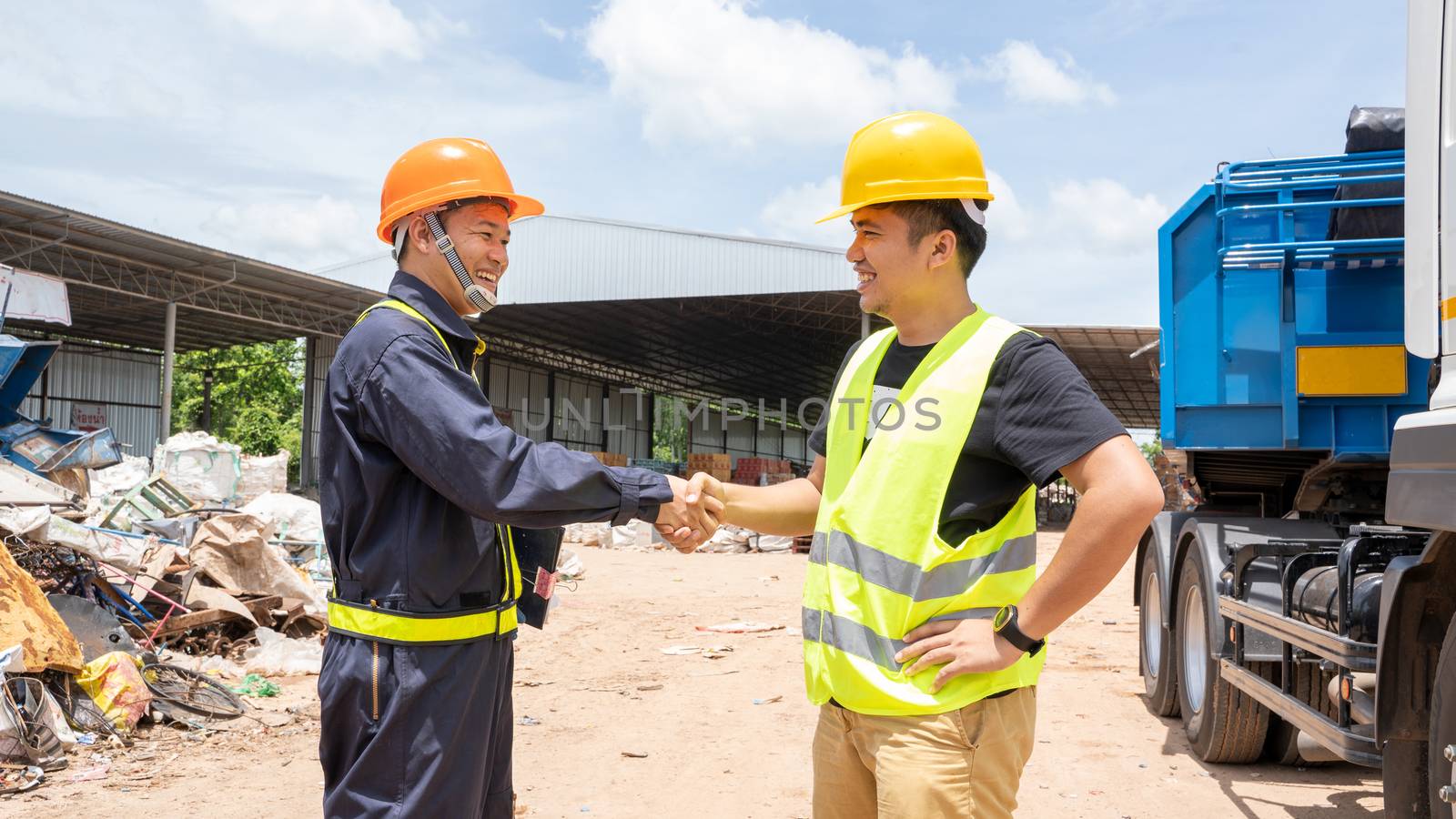 Foreman with safety hats in the parking and shaking hands of two happy young builders while standing at the waste recycling plant.