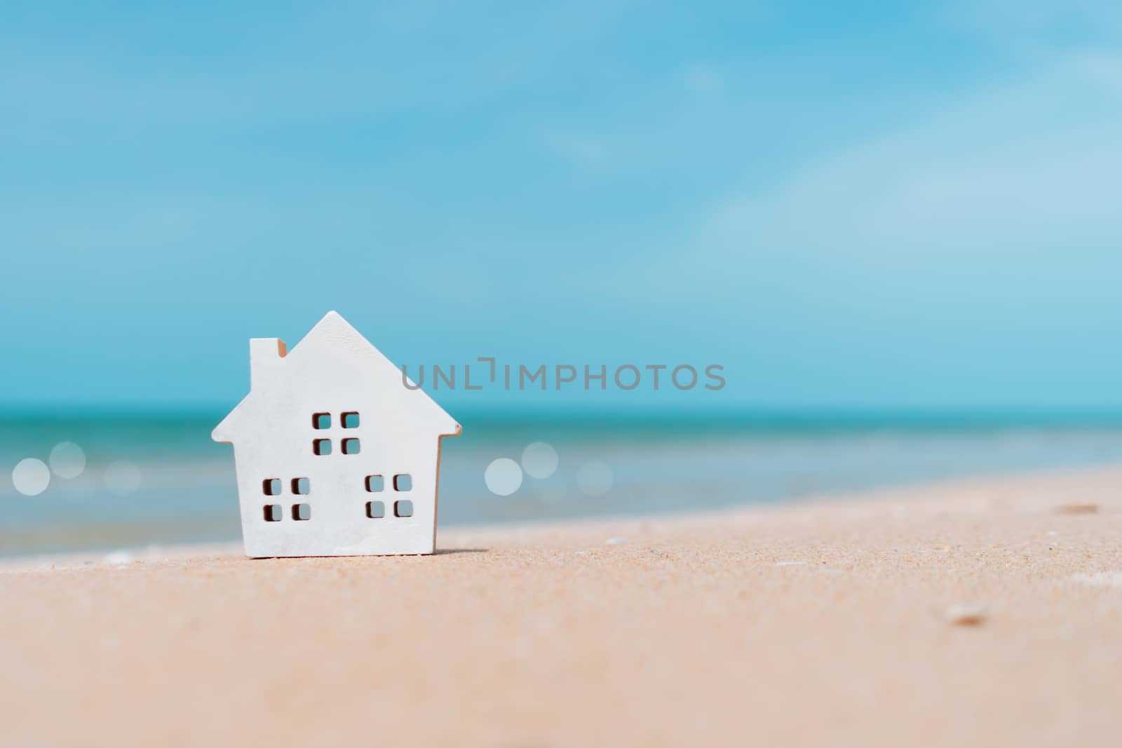 Model of a little house on sand with nature beach background. Dream life concept.