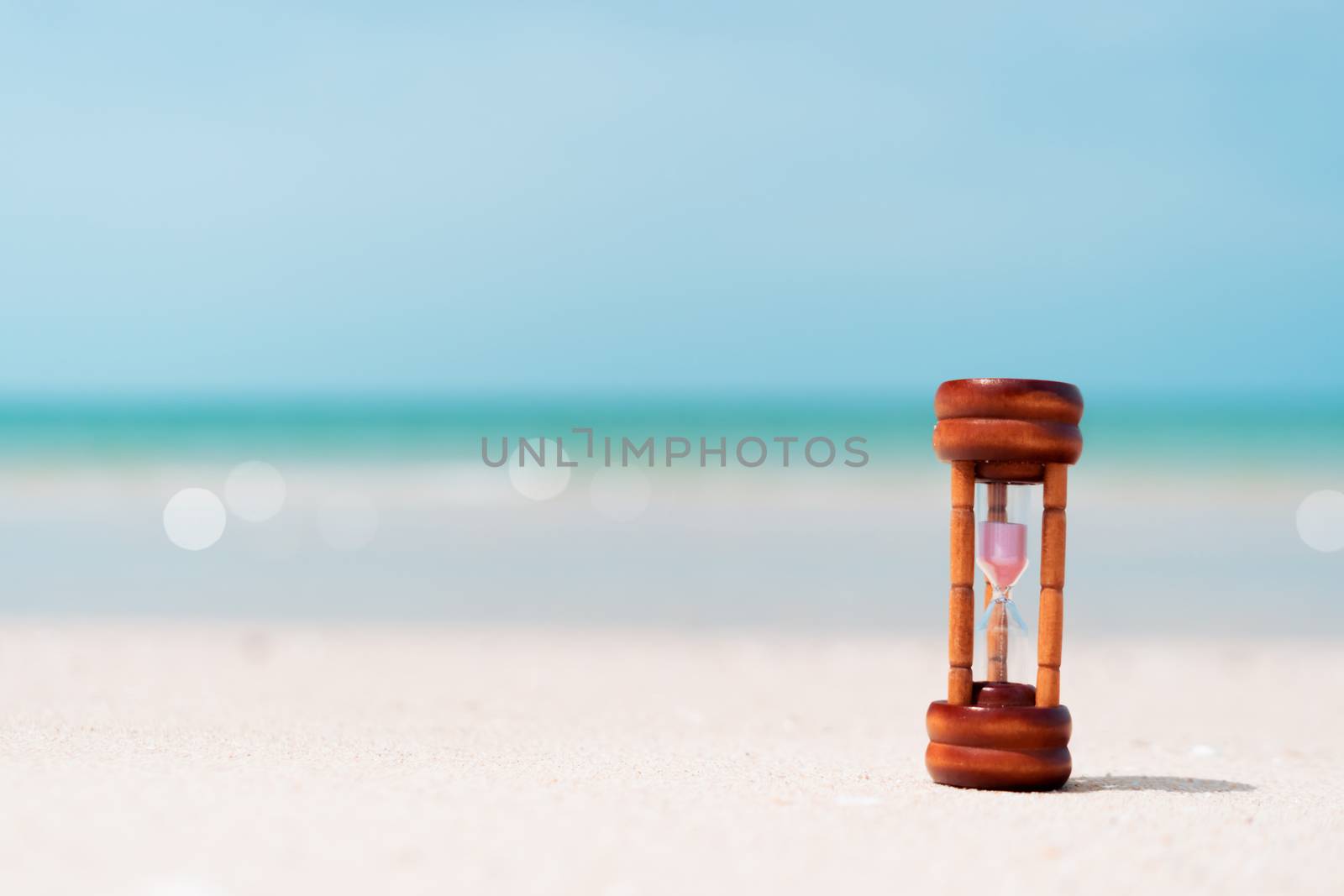 Small hourglass show time is flowing on sand beach texture background.