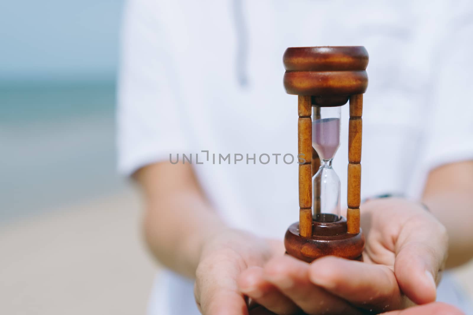 Hand hold small hourglass model show time is flowing on summer beach. by Suwant