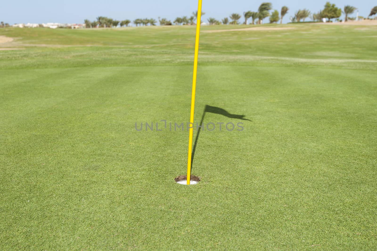 Base of a yellow flag pole in hole on green of golf course with shadow