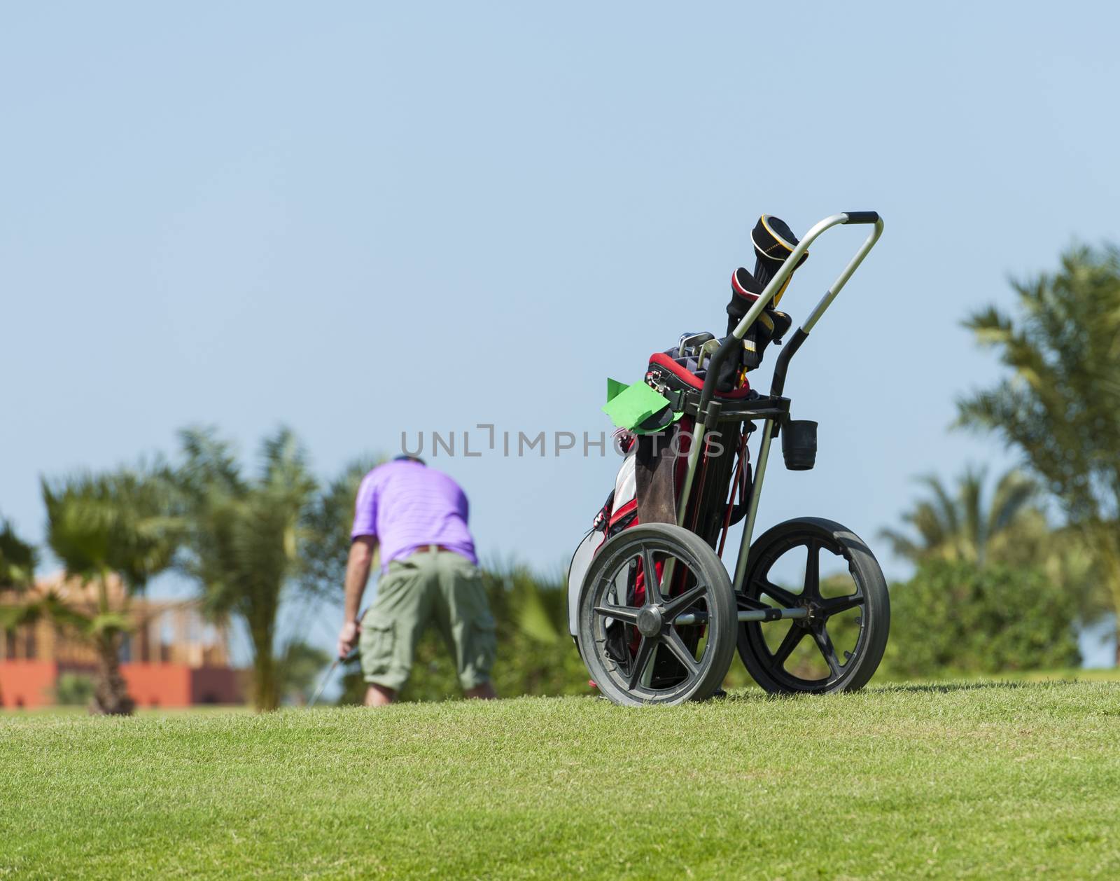 Golf caddy trolley and bag on a golf course with golfer in the distance