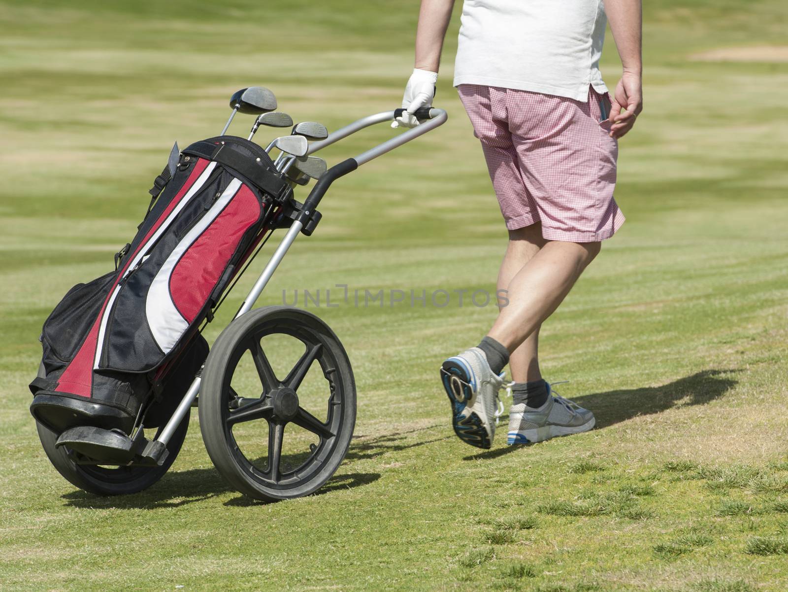 Golfer walking down the fairway on a course with golf bag and trolley