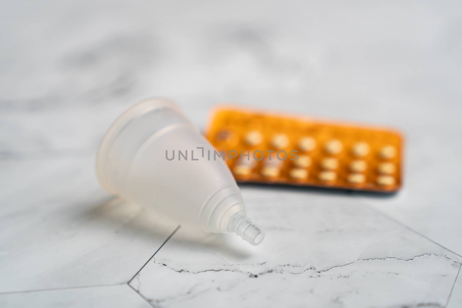 Birth control pill and menstrual cups with on white marble background.