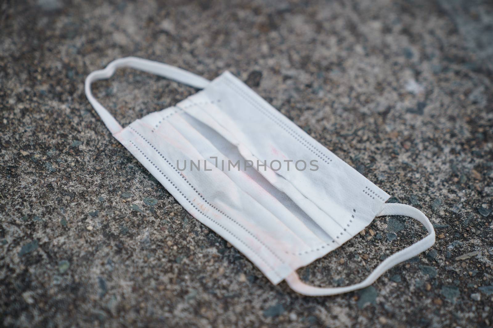 Used dirty face surgical mask dropped on the ground, selective focus center mask