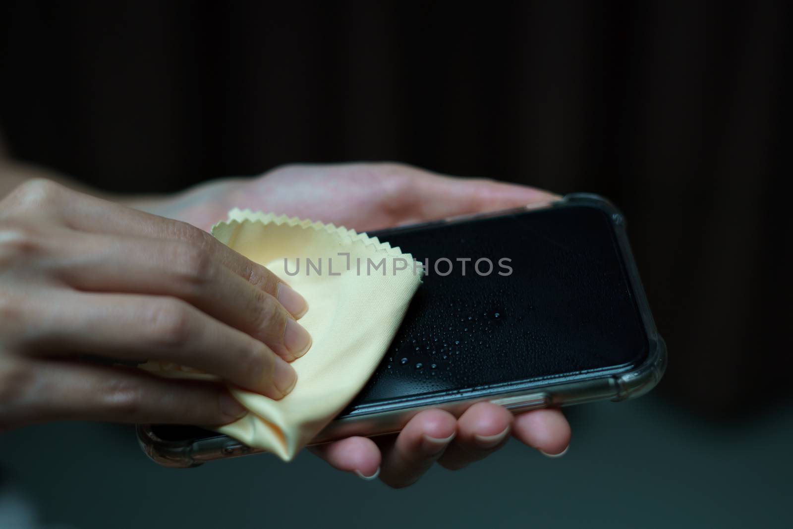 Hand holding and cleaning mobile phone screen with a napkin for corona virus or Covid-19 protection.