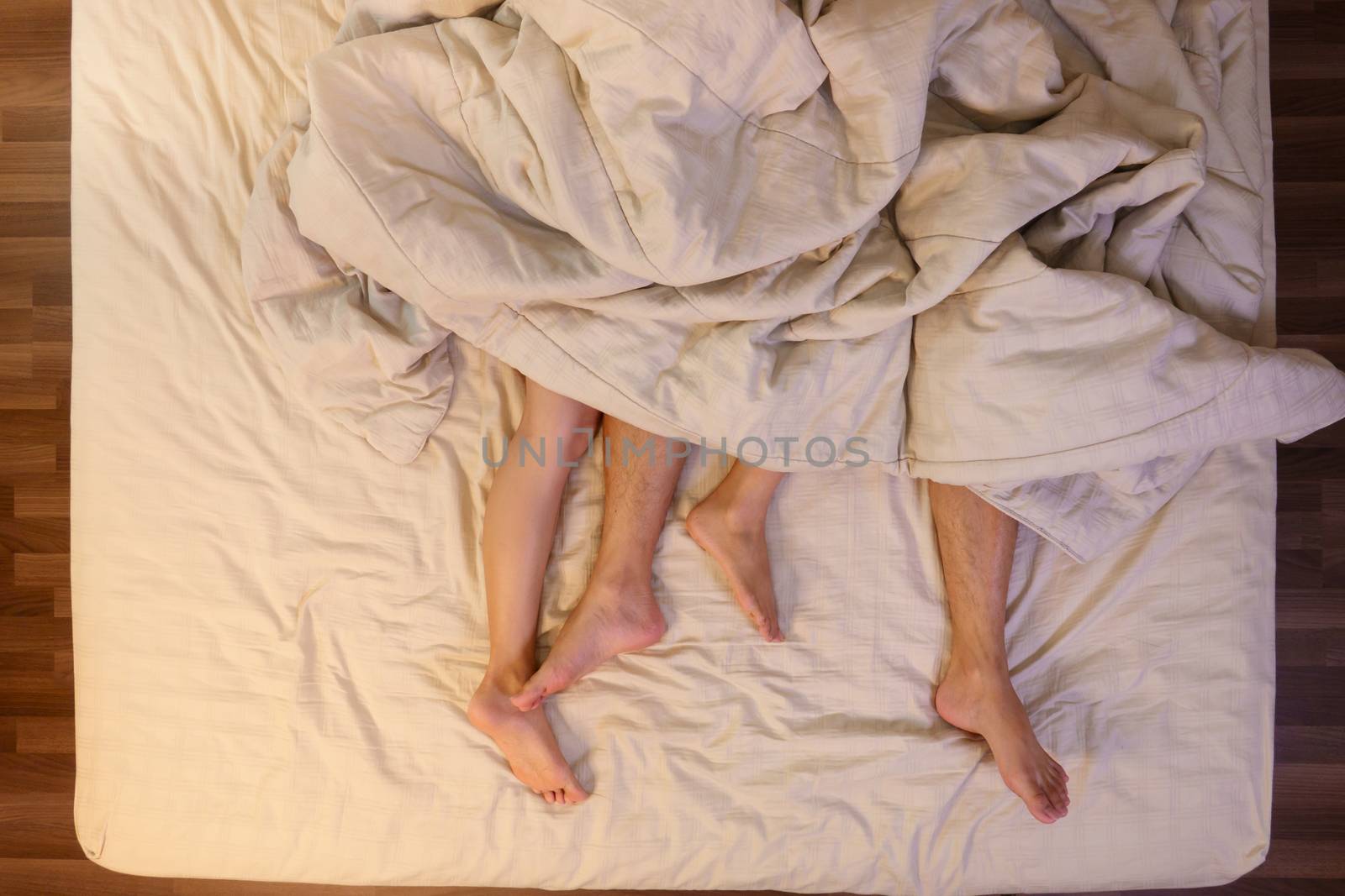 Close up of male and female feet on a bed having sex under sheets in the bedroom.