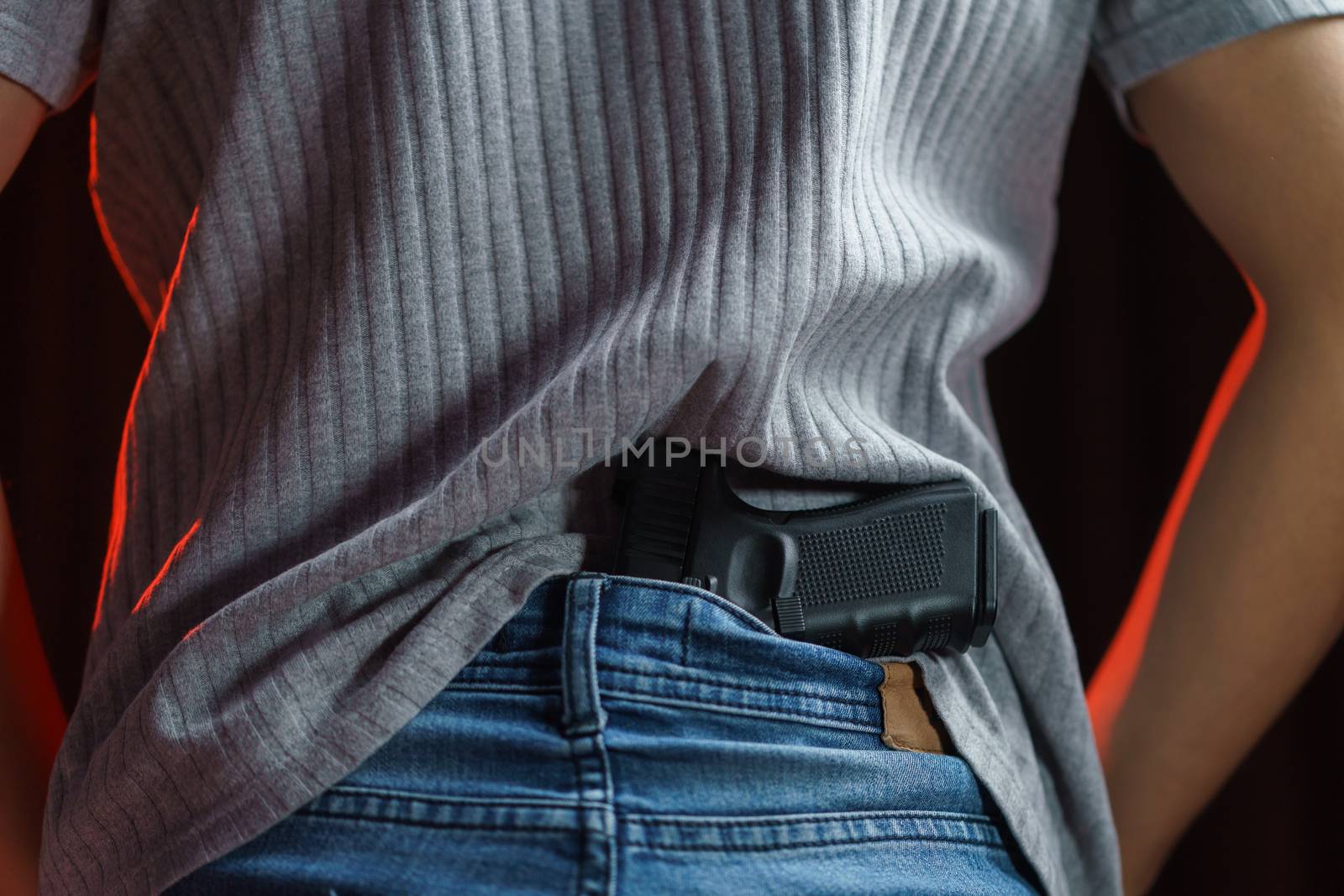 Man hiding his gun in his jeans on black background.