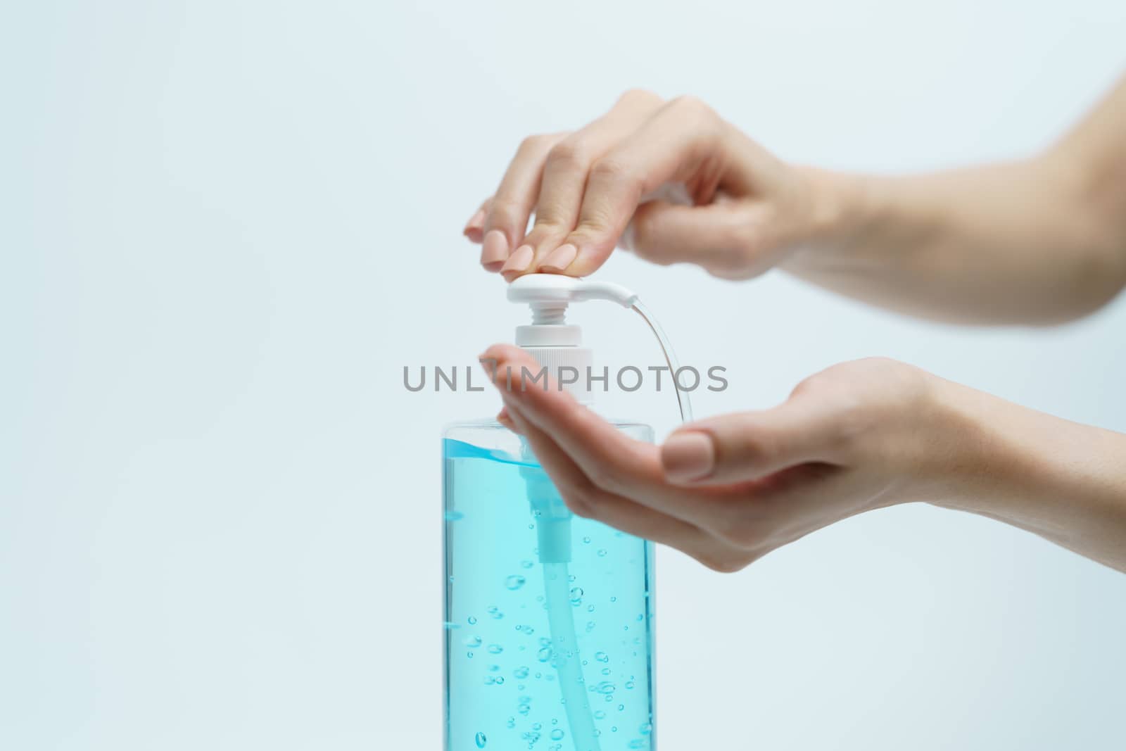 Hand with hand sanitizer in a clear pump bottle on a white background.