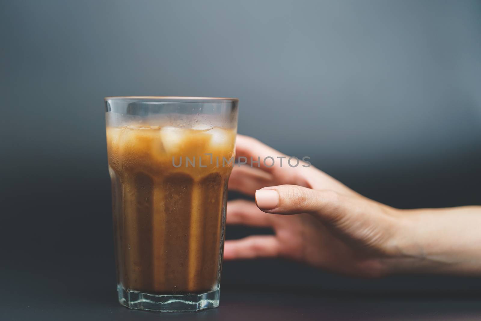 Hand with ice coffee in a tall glass on dark background. by sirawit99
