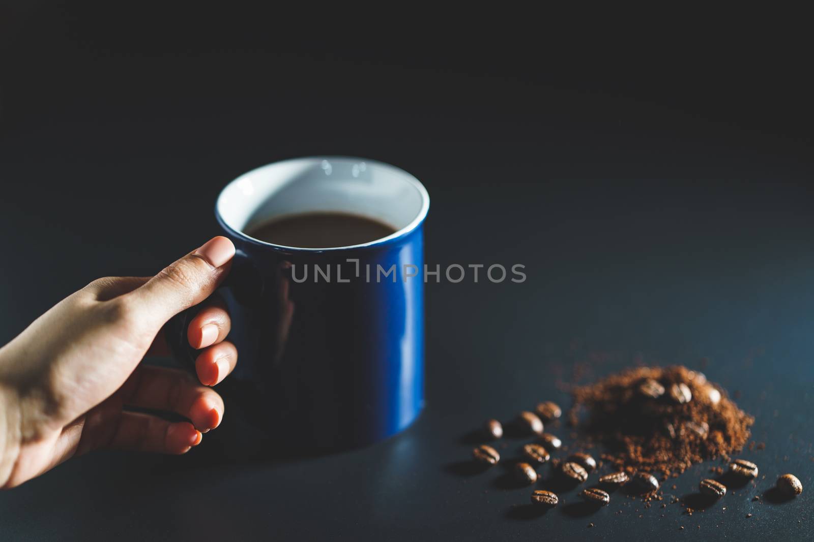 Hand holding a cup of coffee with coffee beans and powder on bla by sirawit99