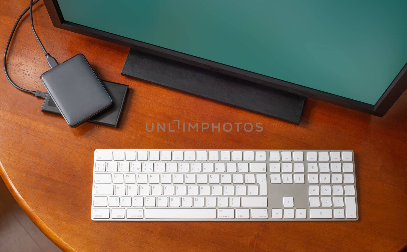 A computer monitor, a digital wireless keyboard and hard disk drives on a round wooden desk