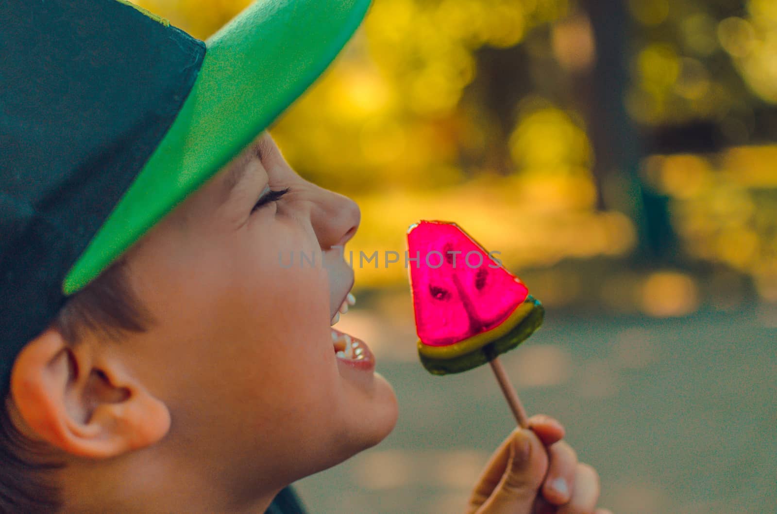 close portrait of laughing boy with red lollipop candy