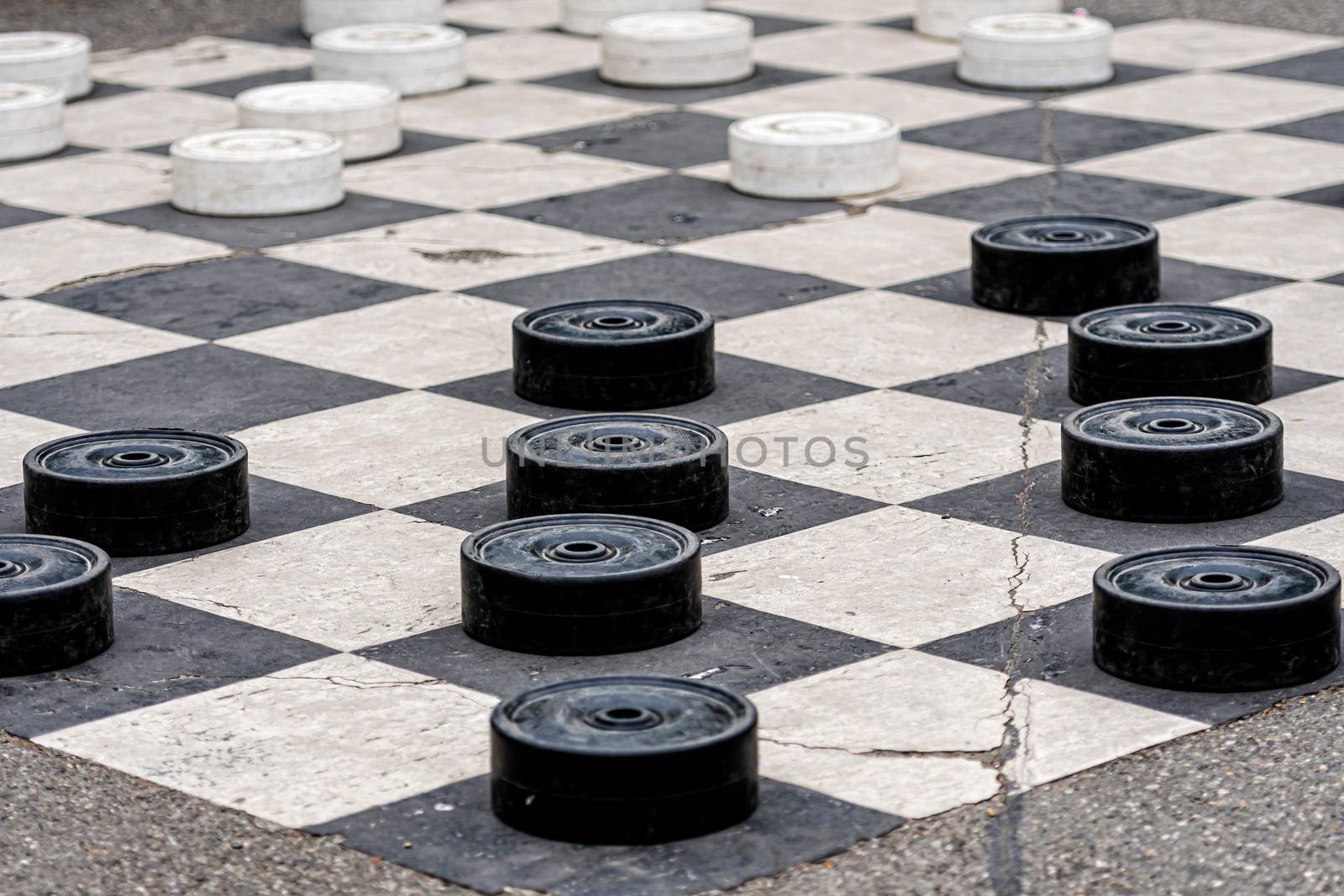 Large plastic checkers painted on the pavement cells in a city park - image