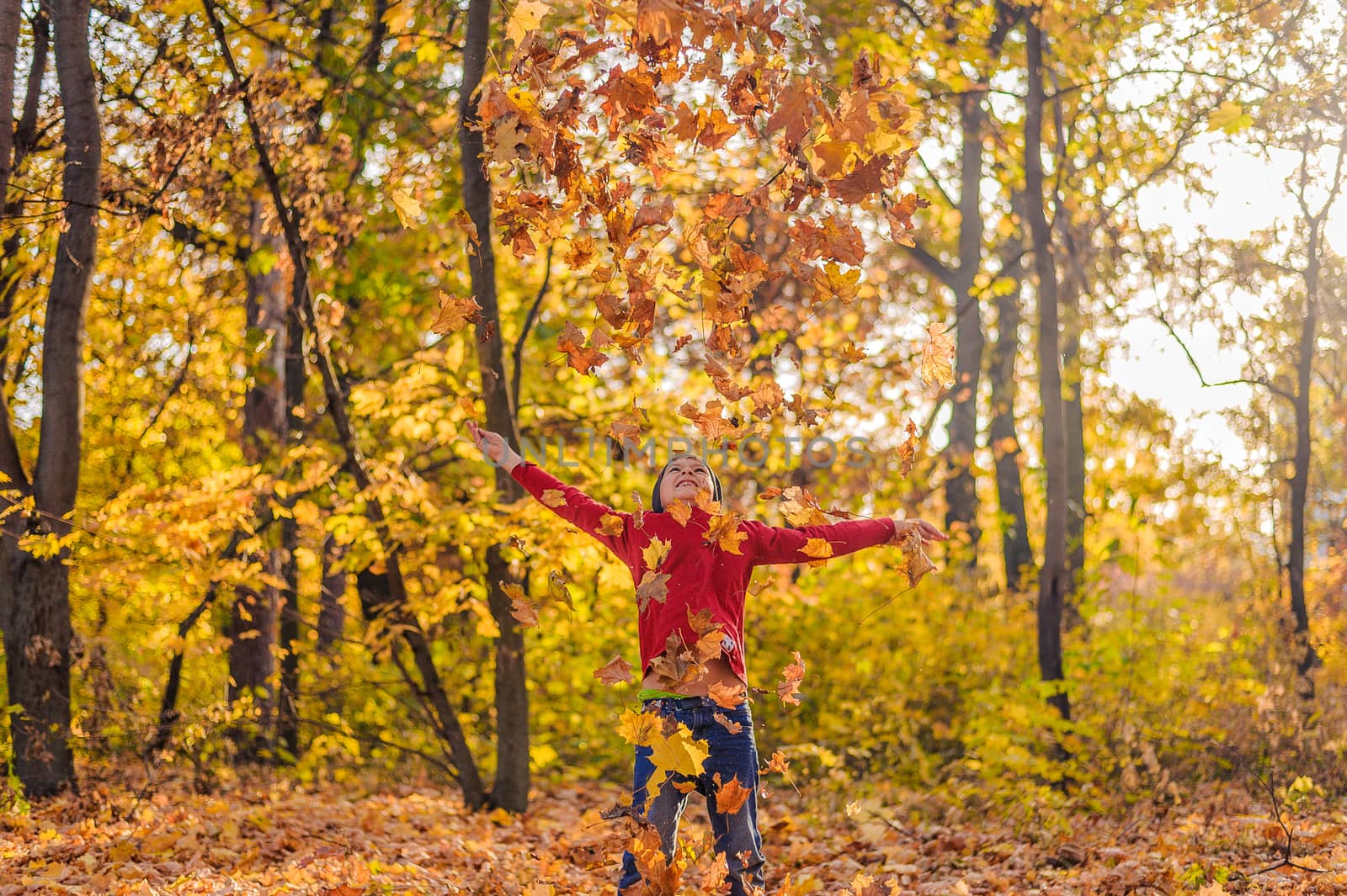 happy boy in a red sweater throws up an armful of yellow leaves in the autumn forest by chernobrovin