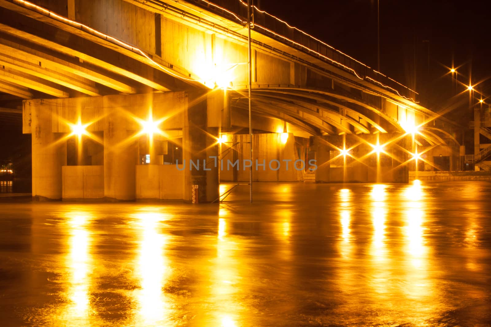The light at night shines under the bridge over the river.