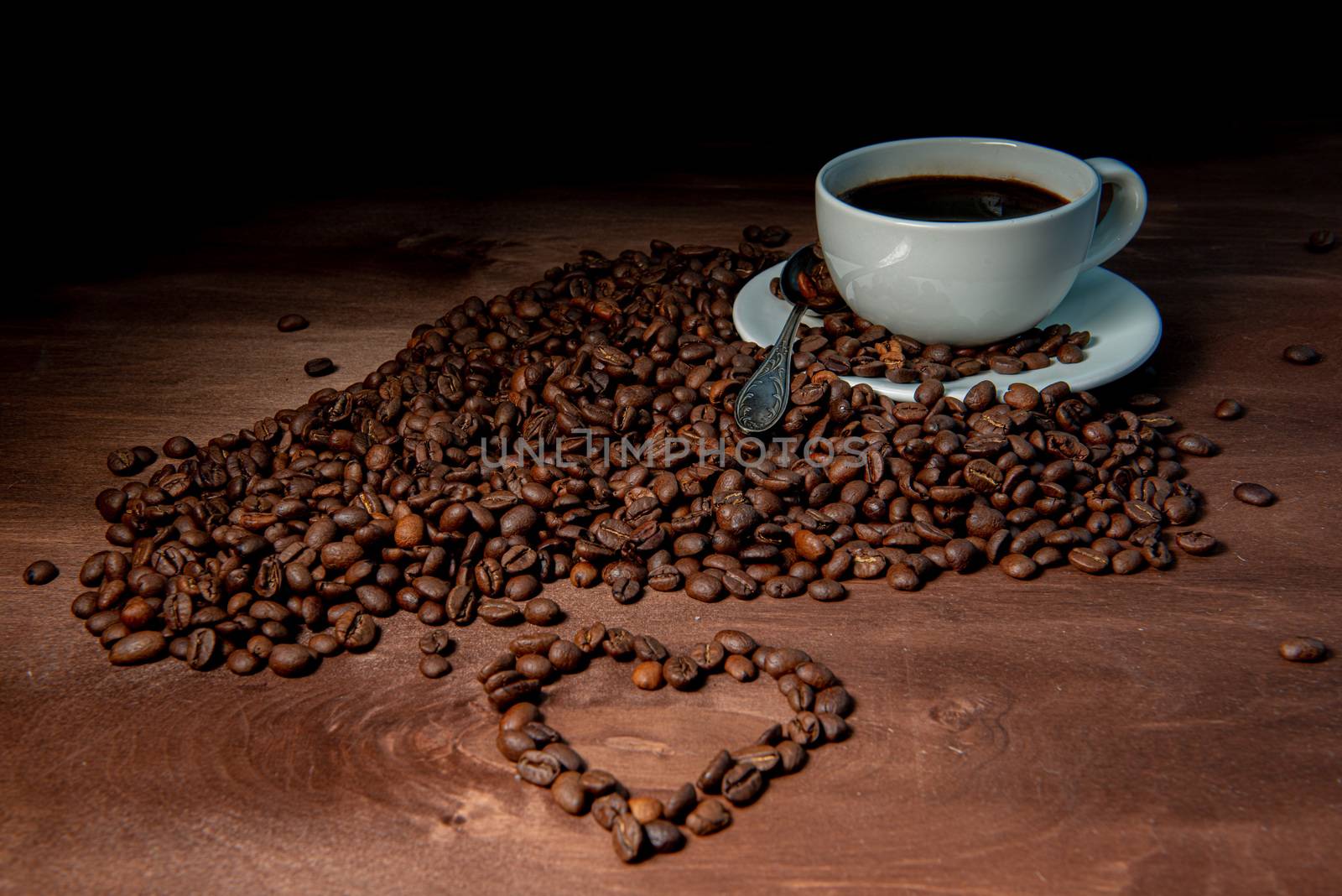 White coffee mug and coffee beans on the dark wooden background, Heart shape from coffee beans in the foreground - image