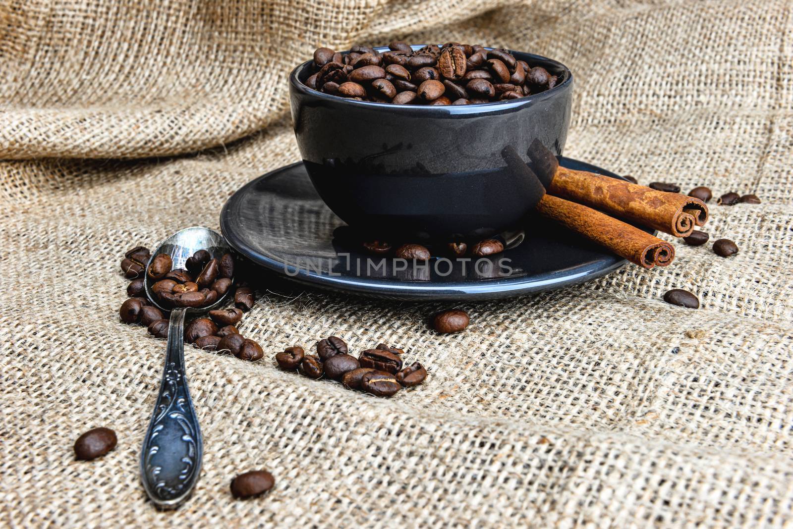 Black coffee mug full of organic coffee beans and  cinnamon sticks on linen cloth - image