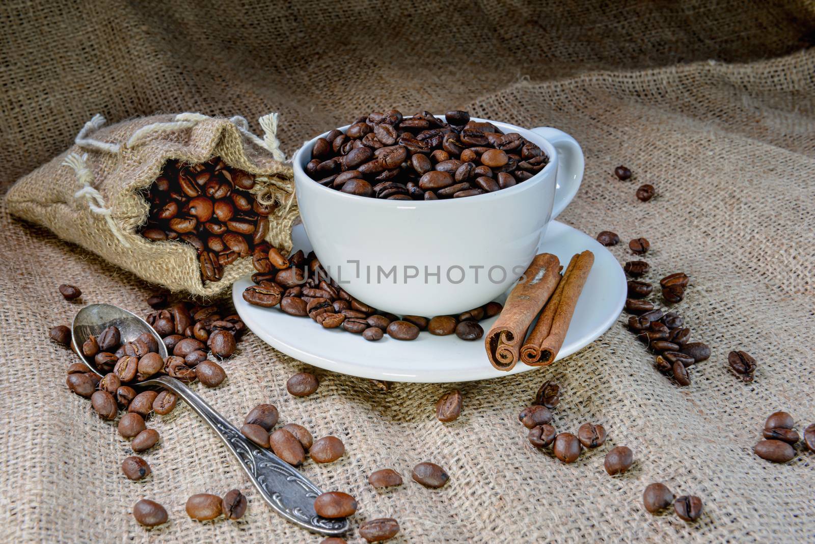 White coffee mug full of organic coffee beans and  cinnamon sticks on linen cloth - image