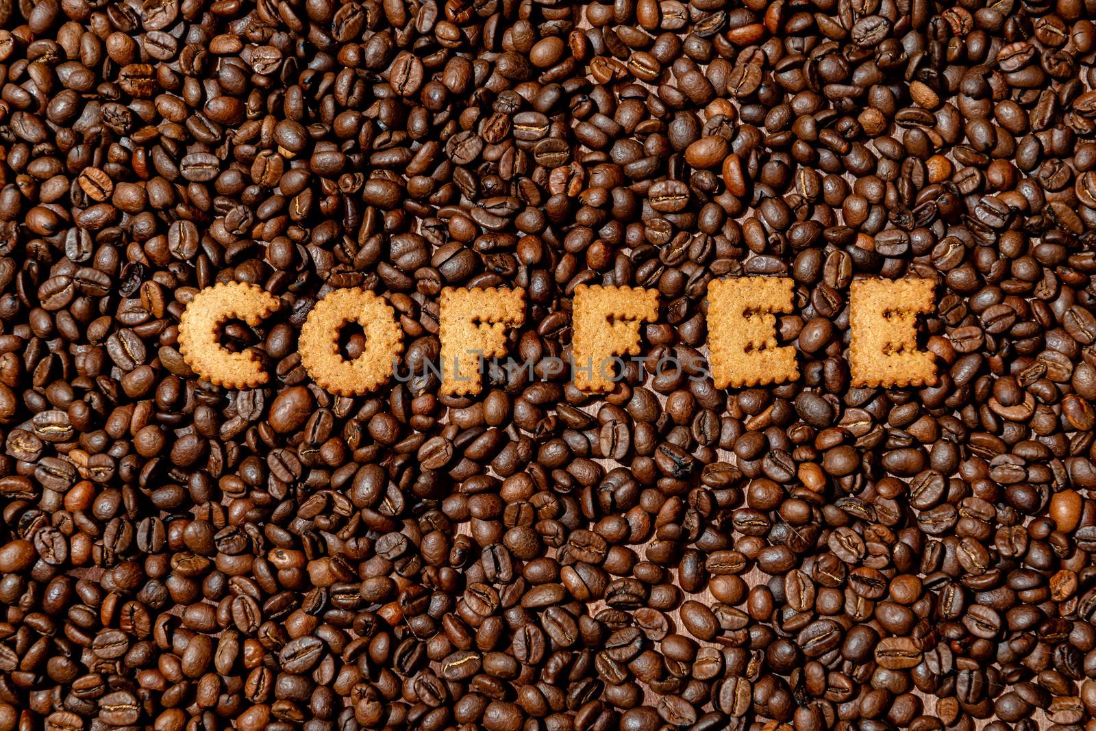 The word COFFEE  made from biscuit letters on a dark coffee bean background - image