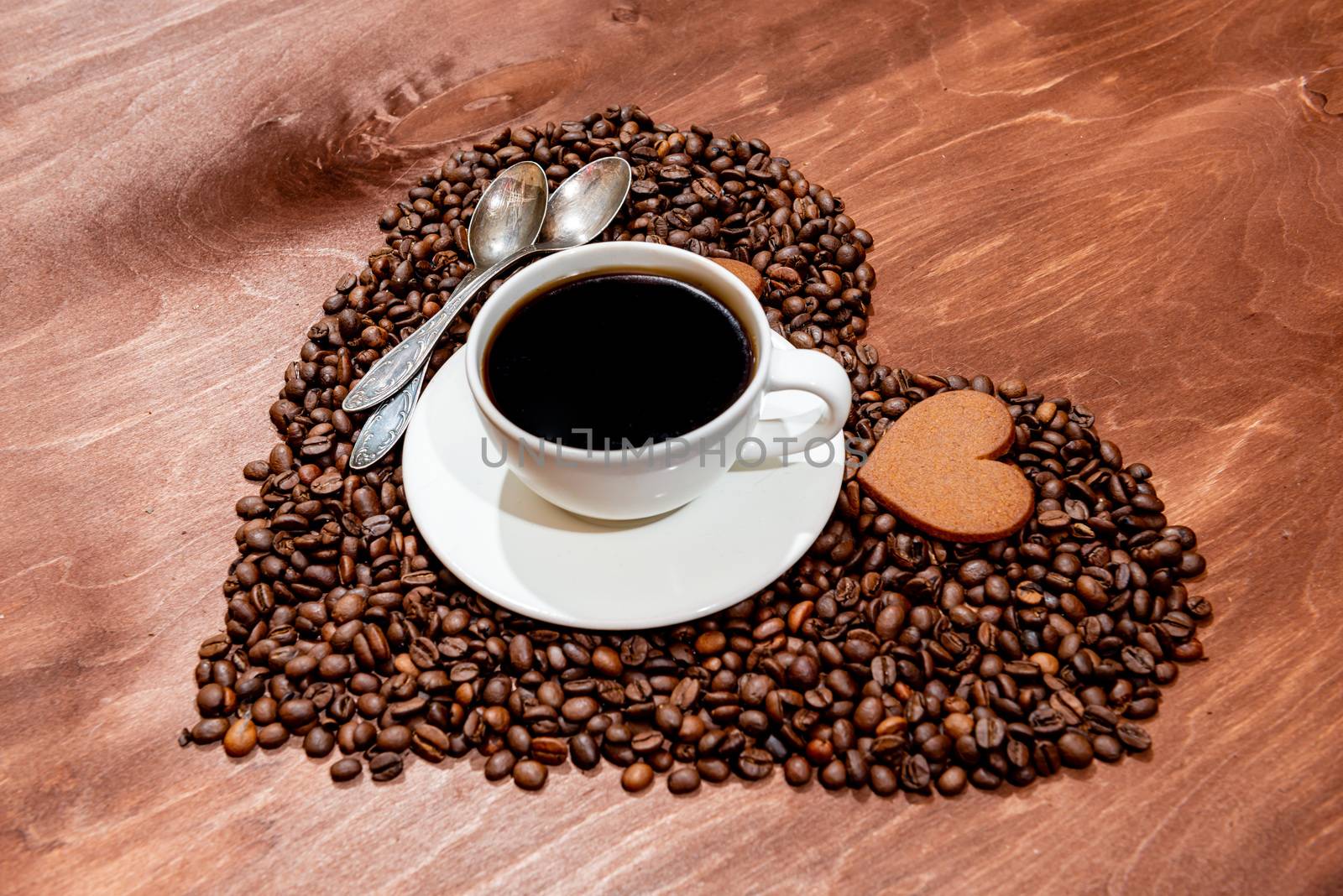 White coffee mug, heart shaped gingerbread and two spoons on a heart shaped base made from coffee beans - image