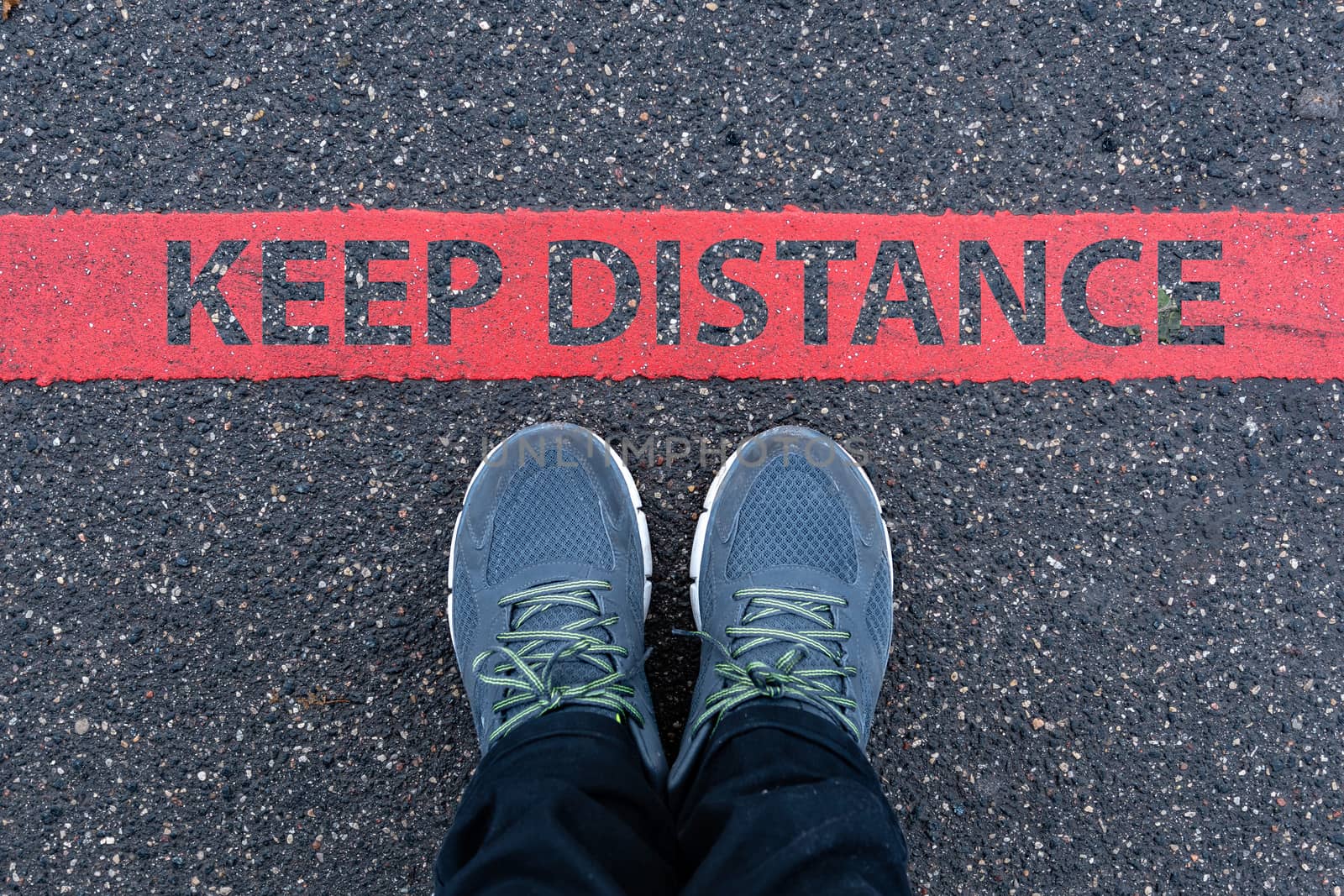 man in sneakers standing next to a red line with text KEEP DISTANCE, restriction or safety warning concept